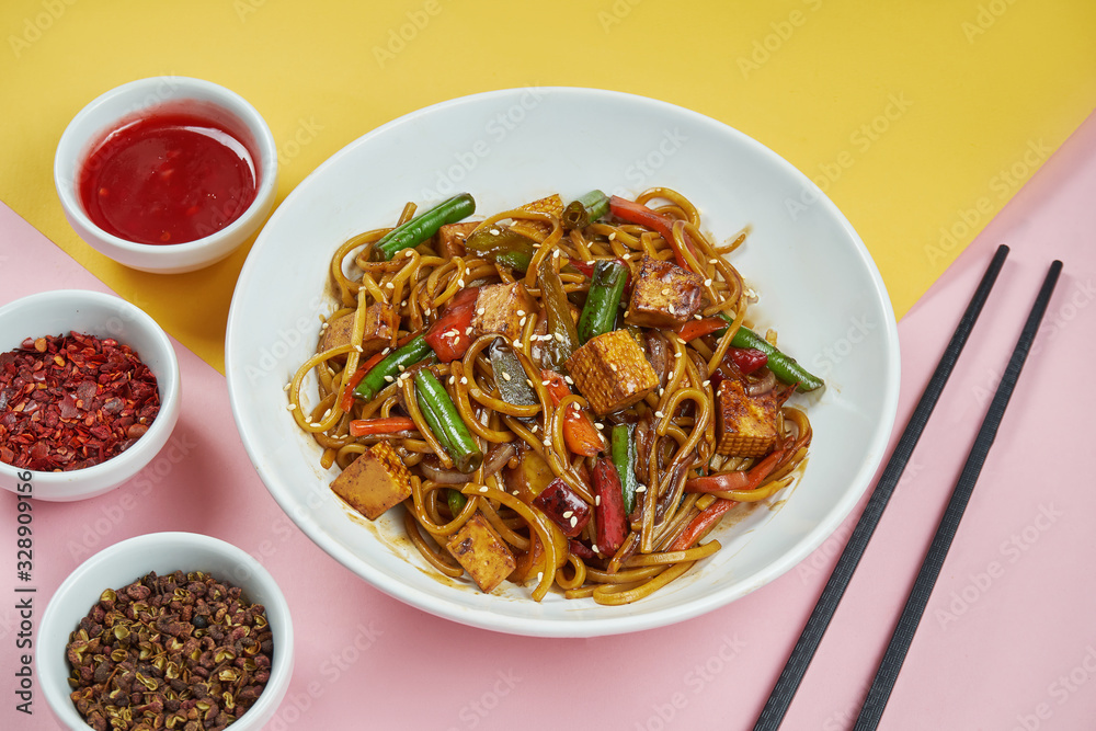 Appetizing homemade egg noodles in sweet and sour sauce with tofu and vegetables in a white bowl on colored background. Close up. Asian cuisine Appetizing homemade egg noodles in sweet and sour sauce with tofu and vegetables in a white bowl on colored background. Close up. Asian cuisine
