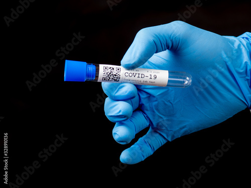 Test tube sample COVID-19 test in hand or researcher in rubber glove on black background