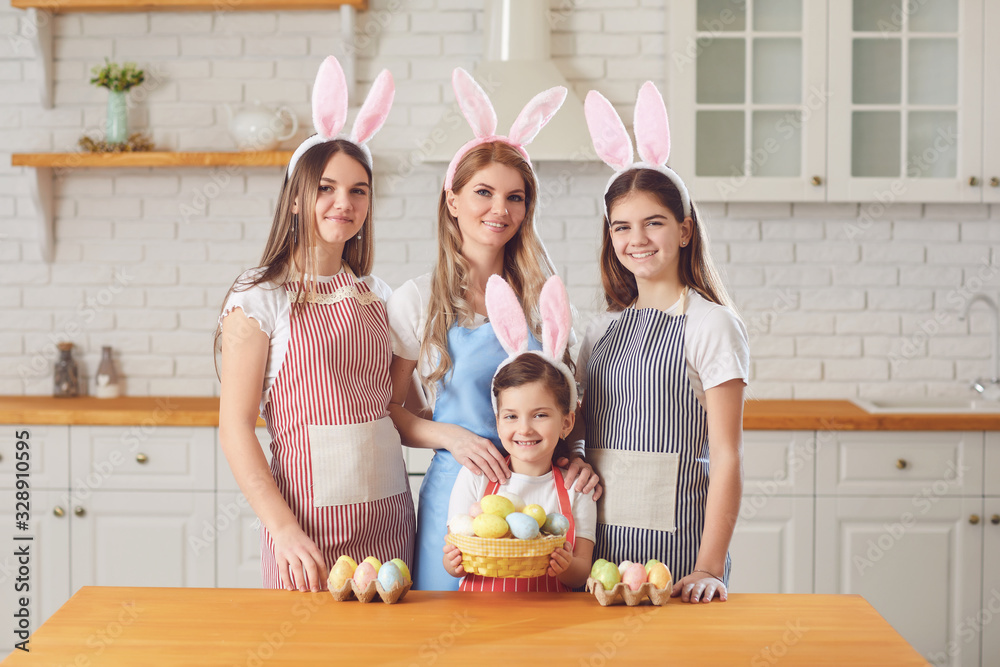 Fototapeta premium Happy easter. Mother and daughters with rabbit ears decorate Easter eggs at a table in kitchen.
