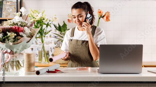 Female florist standing in flower shop. Young woman talking on mobile phone. photo