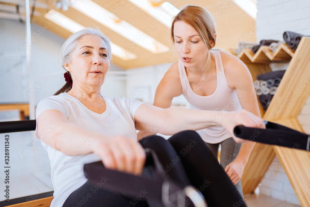Personal trainer assist senior woman exercising on machine at gym Personal trainer assist senior woman exercising on machine at gym
