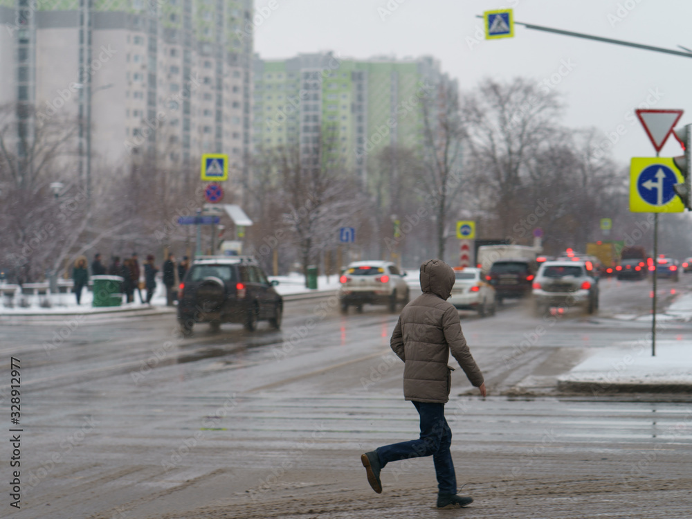 Young man crossing the road in winter day. Lifestyles of big city concepts. Defocused photography of people on the bus stop as background.