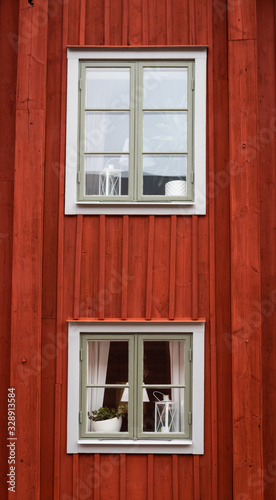 Old red plank wood swedish cottage windows with white frame. Curtains and laps in the windows