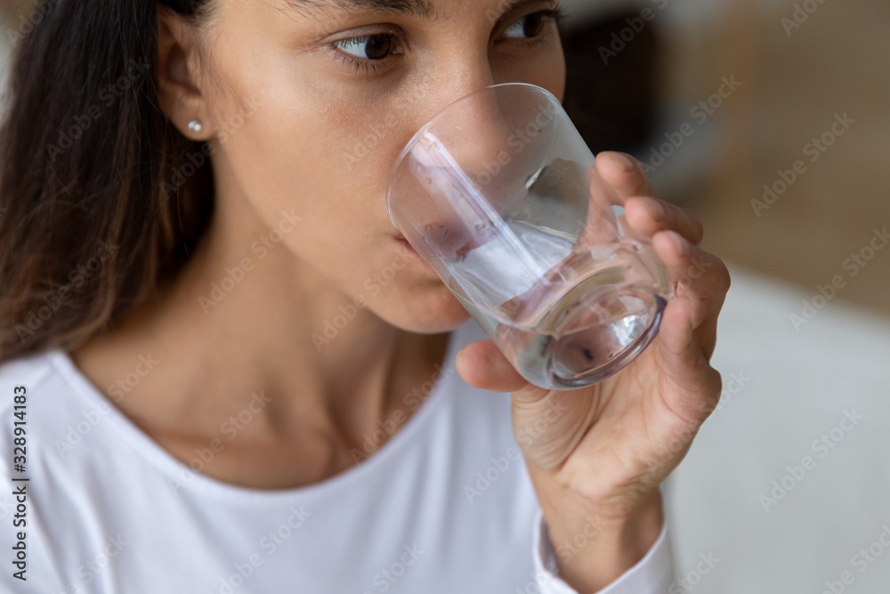 Close up of young Caucasian woman hold glass drinking pure mineral water maintain body balance, millennial girl enjoy clear still aqua fell thirsty at home, healthy lifestyle, good habit concept Close up of young Caucasian woman hold glass drinking pure mineral water maintain body balance, millennial girl enjoy clear still aqua fell thirsty at home, healthy lifestyle, good habit concept