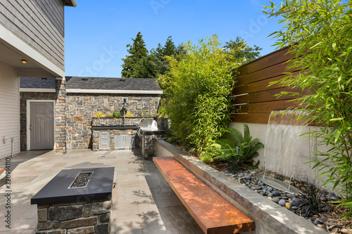 Home exterior backyard hardscape entertainment area with fire pit, bench seating, water feature and barbecue photo
