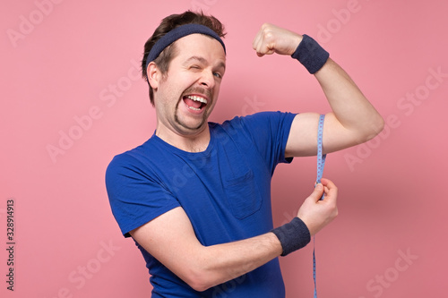 Young handsome funny man wearing blue t-shirt, holding his arm up to show how strong he