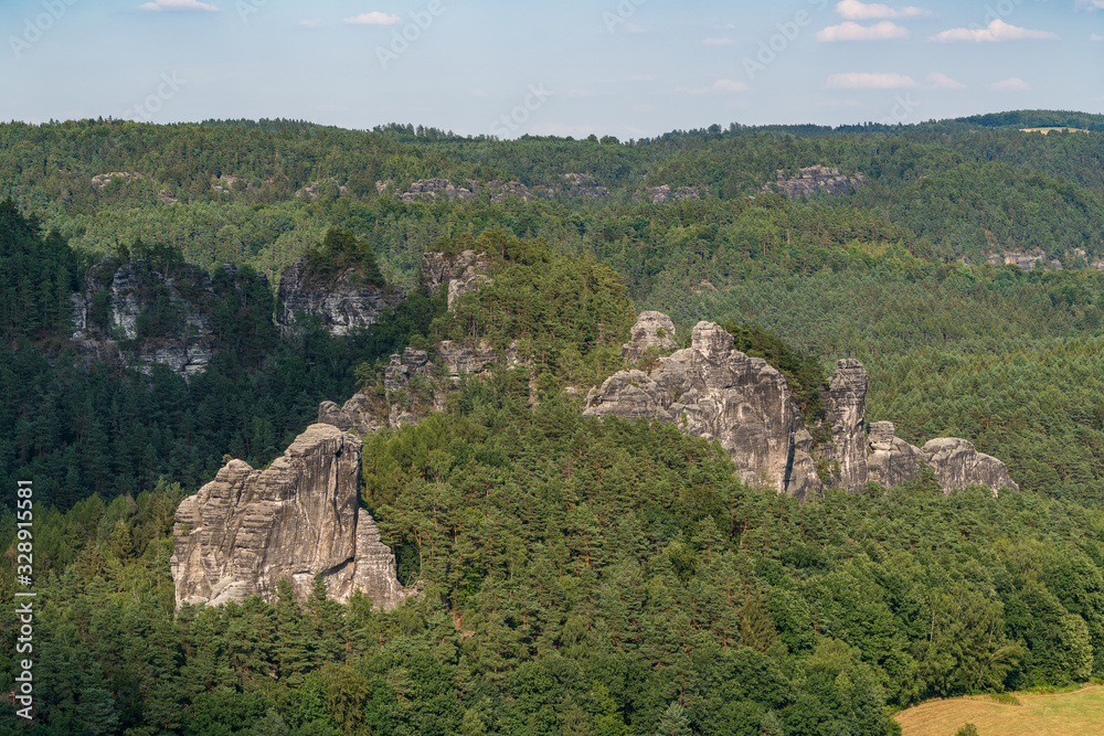 Bad Schandau in Bohemian Switzerland. Bastei bridge and mountain view. Narrow rock, natural sandstone arch in Europe..Hill scenery with greenery, blue sky and sunlight. Bad Schandau in Bohemian Switzerland. Bastei bridge and mountain view. Narrow rock, natural sandstone arch in Europe..Hill scenery with greenery, blue sky and sunlight.
