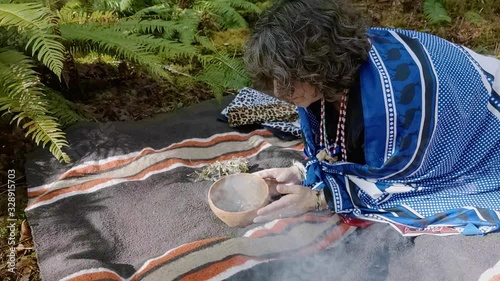Woman shaman on a blanket burning plant medicine in a clay bowl talking with her ancestors photo