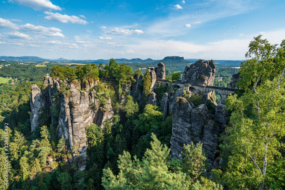 Obraz premium Bad Schandau in Bohemian Switzerland. Bastei bridge and mountain view. Narrow rock, natural sandstone arch in Europe..Hill scenery with greenery, blue sky and sunlight.