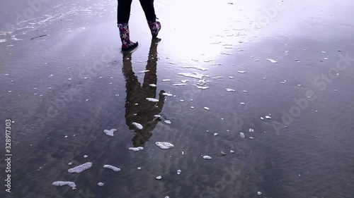 Reflection of a woman walking in rubber boots on the beach
