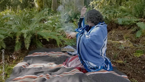 Woman shaman smudging her chakras using natural plants, lush green rainforest