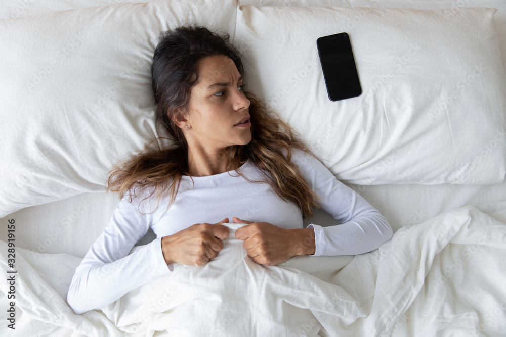 Φωτογραφία Top view of depressed Caucasian young woman lying in white cozy bed at home look