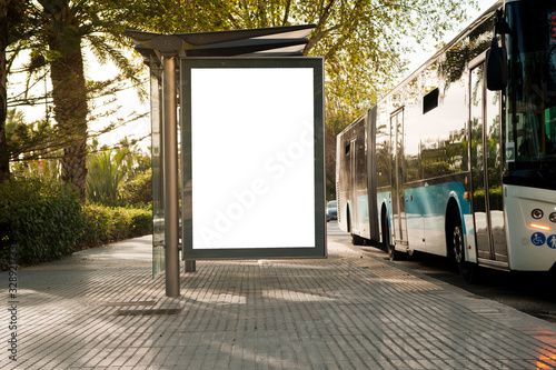 White blank vertical billboard at the bus stop on the city street. In the background of buses and roads. Sketch. Poster on the street next to the road.