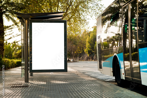 White blank vertical billboard at the bus stop on the city street. In the background of buses and roads. Sketch. Poster on the street next to the road.