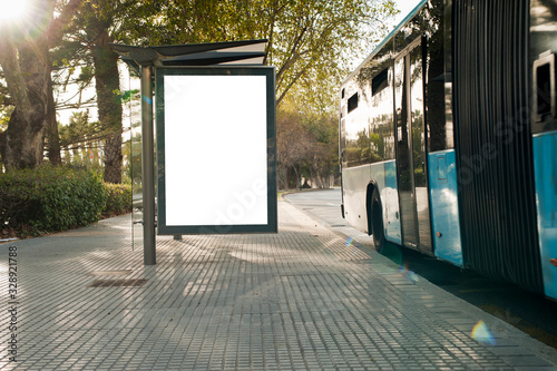 White blank vertical billboard at the bus stop on the city street. In the background of buses and roads. Sketch. Poster on the street next to the road.