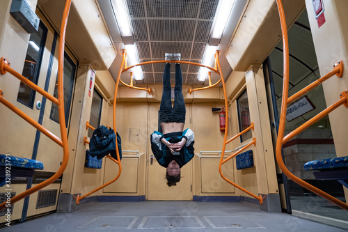 Bild auf Leinwand Girl hanging by feet upside down in the subway carriage and using smartphone