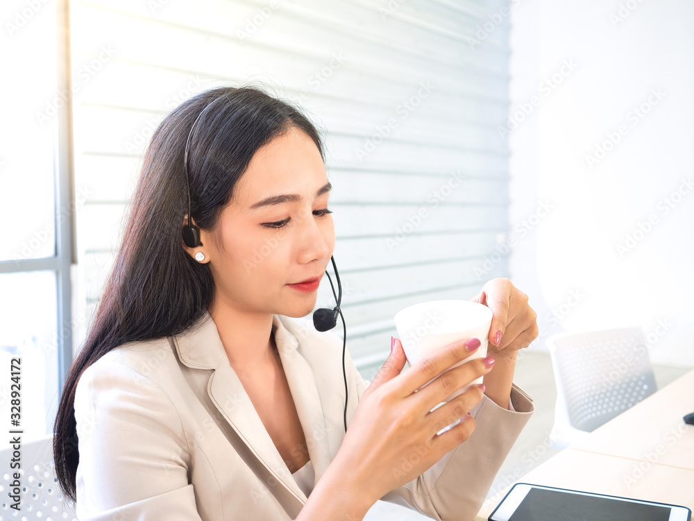 Asian professional businesswoman call center rest, relax and peaceful in break time by drink coffee or tea in white ceramic cup after support and service client by communicate from microphone headset Asian professional businesswoman call center rest, relax and peaceful in break time by drink coffee or tea in white ceramic cup after support and service client by communicate from microphone headset