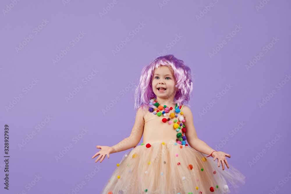 Childrens birthday party, masquerade. Little happy toddler child girl in a puffy tutu fancy dress, having fun on Violet background. Space for text