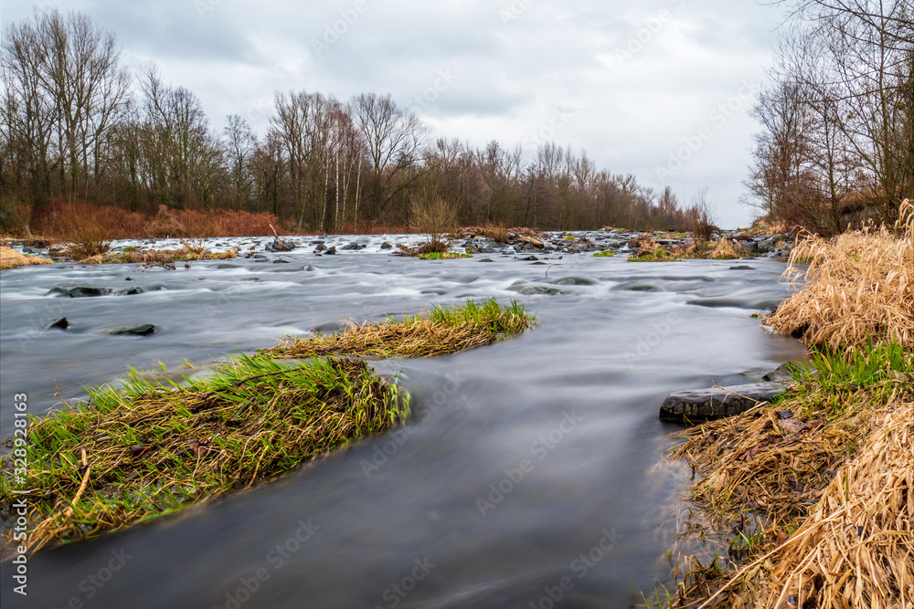 Long exposure of a river with trees in the background during a rainy autumn day Long exposure of a river with trees in the background during a rainy autumn day