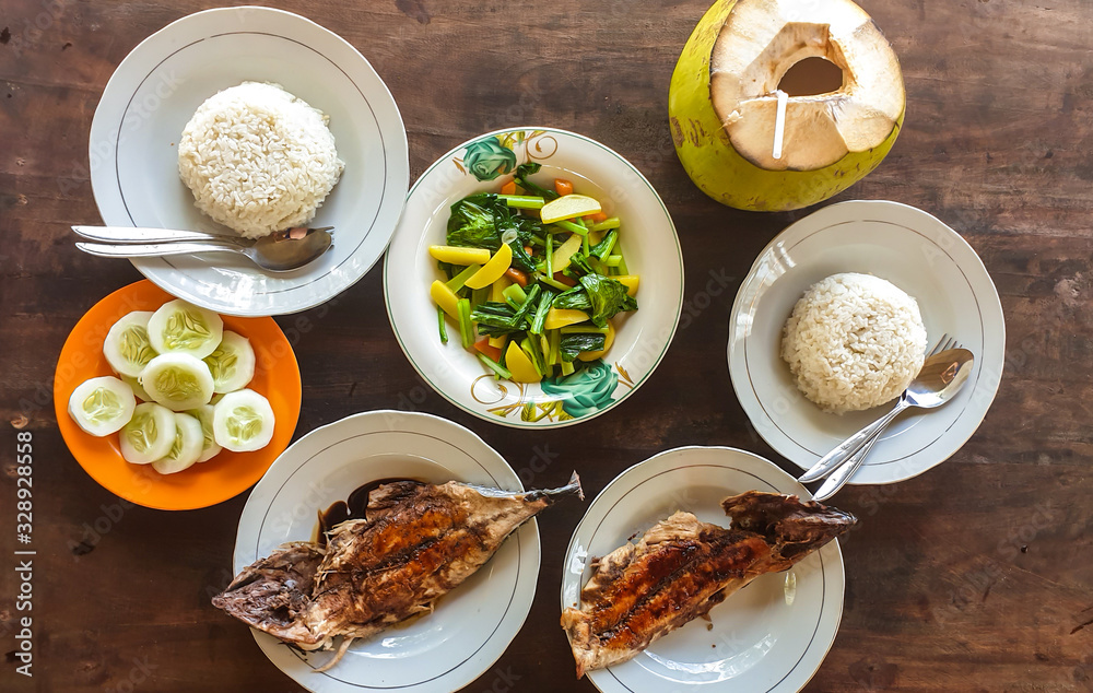 Island style dinner served directly at the seashore on Koka Beach, Flores, Indonesia. The meal consist of grilled fish, rice and steamed vegetables. There is also a fresh coconut juice. Healthy meal