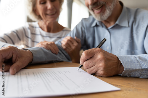 Close up of 60s husband and wife sit at desk sign health insurance contract close deal, smiling old mature couple spouses put signature on document make good agreement, elderly healthcare concept photo