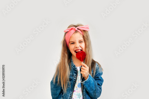 Portrait of a beautiful stylish fashionable girl in glasses, with a heart-shaped lollipop, on a white background, free time summer vacation #328930970