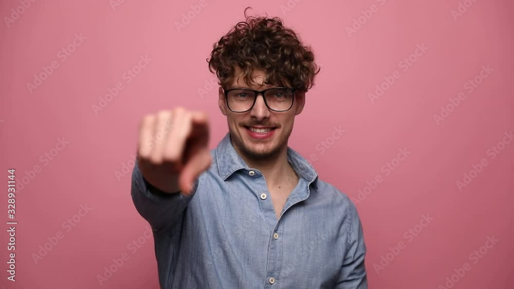 young casual man wearing glasses standing and smiling happy then pointing forward with one hand then with two hands on pink studio background