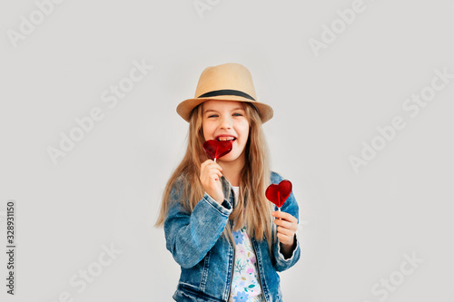 Portrait of a beautiful stylish fashionable girl in glasses, with a heart-shaped lollipop, on a white background, free time summer vacation #328931150