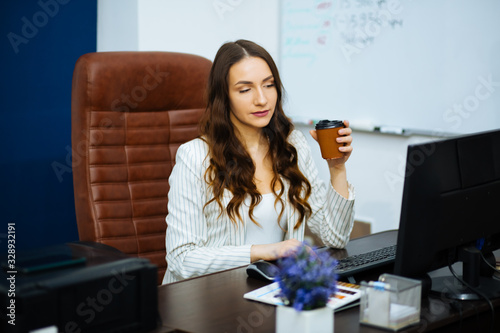 Schilderij op canvas young business lady in white suit at her desk holds a cup of coffee in her hand