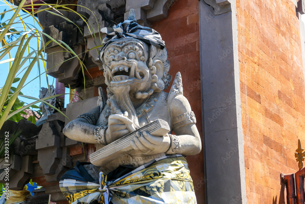 Fototapeta premium A close up on a guardian figure next to a Hindu temple on Bali, Indonesia. The figure is wrapped in checked material tied with yellow ribbon. Tradition and history.