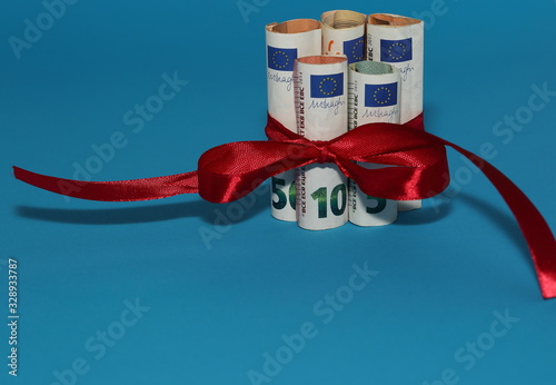 Euro banknotes rolled in rolls and tied with red ribbon bow on blue background, concept of economical financial gift present photo