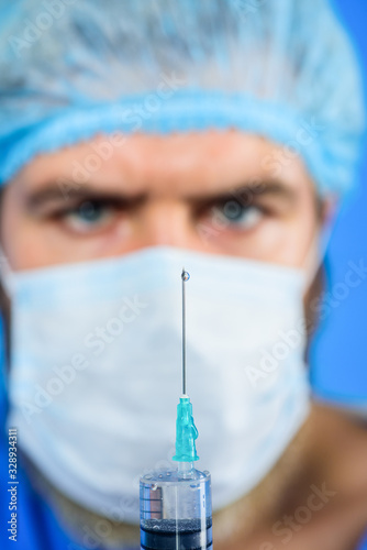 Injection. Professional doctor with medical syringe in hands ready for injection. Doctor with syringe is preparing for injection. Doctor in medical mask holds syringe with vaccine. Selective focus.
