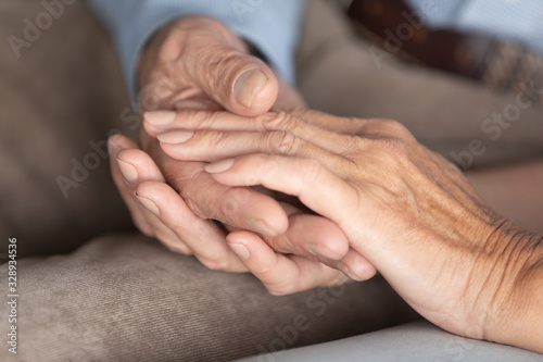 Close up of middle-aged 60s husband and wife hold hands show support and care, loving mature elderly couple embrace cuddle sharing having tender close romantic moment at home, relationships concept