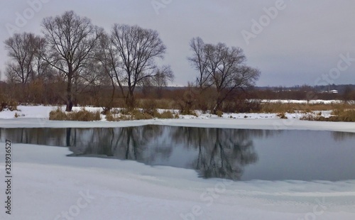 Beginning of spring .Frozen river with a water glade.Snowy bank © Ирина Кузина
