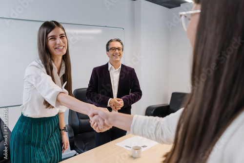 Candid smile and friendly handshake between HR manager and job applicant with smiling senior recruiter in the background