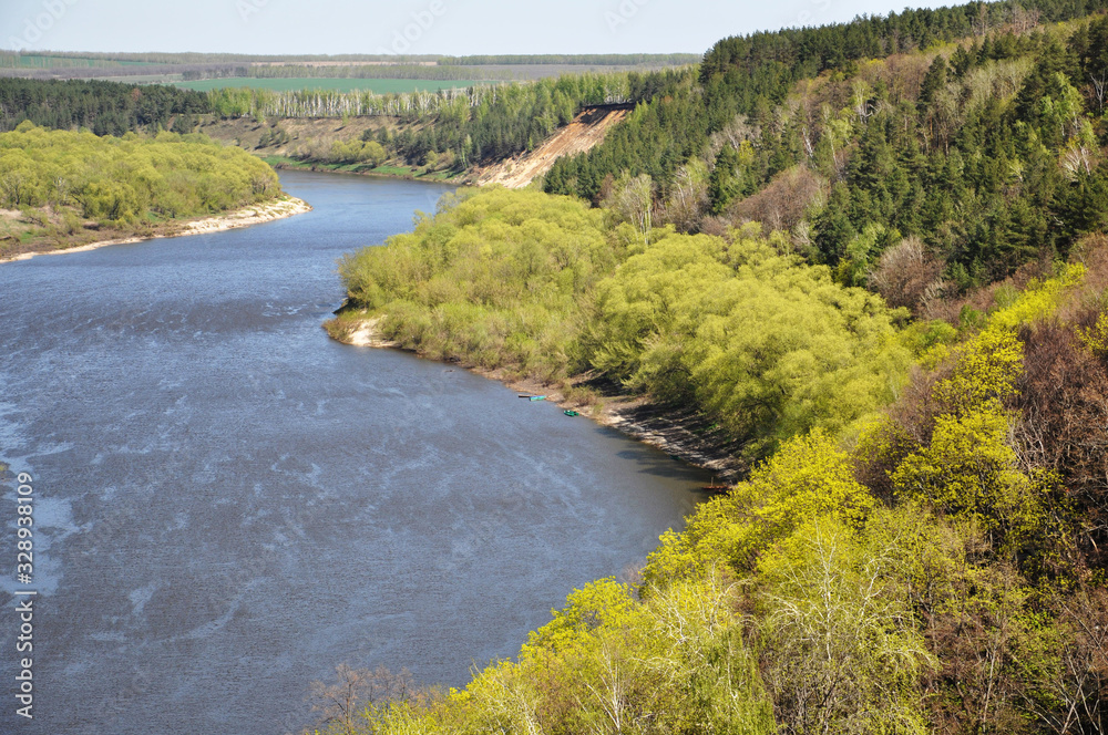 Spring scenery . Panoramic top view of the bend of a large river. Trees with young foliage grow along the banks of the river. Forest and field are visible in the distance.