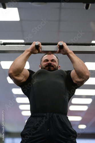 chin up on bar of young strong caucasian man with beard in bright sport gym during hard workout