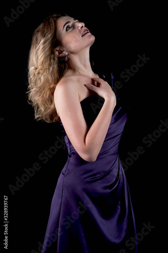 side view of beautiful confident woman with long hair in purple bare shoulder dress holding hand on chest and looking up on black
