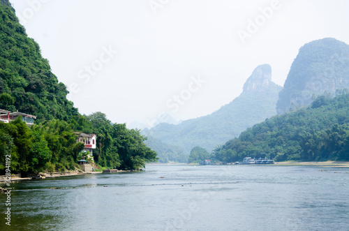 The Li River at Yangshuo, Guilin, China, with a house, distant buildings and karst mountains hiding in the mist on the horizon
