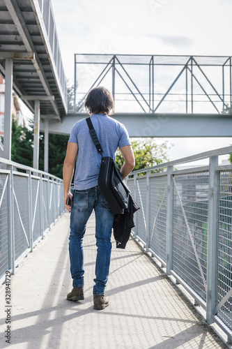 Man dressed in jeans and blue shirt carries a black wallet and climbs up a metal walkway