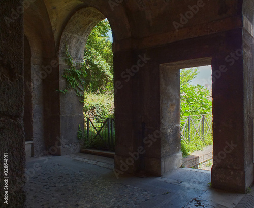 View on an entrance and an arc. Green trees and plants behind them. Old architecture.