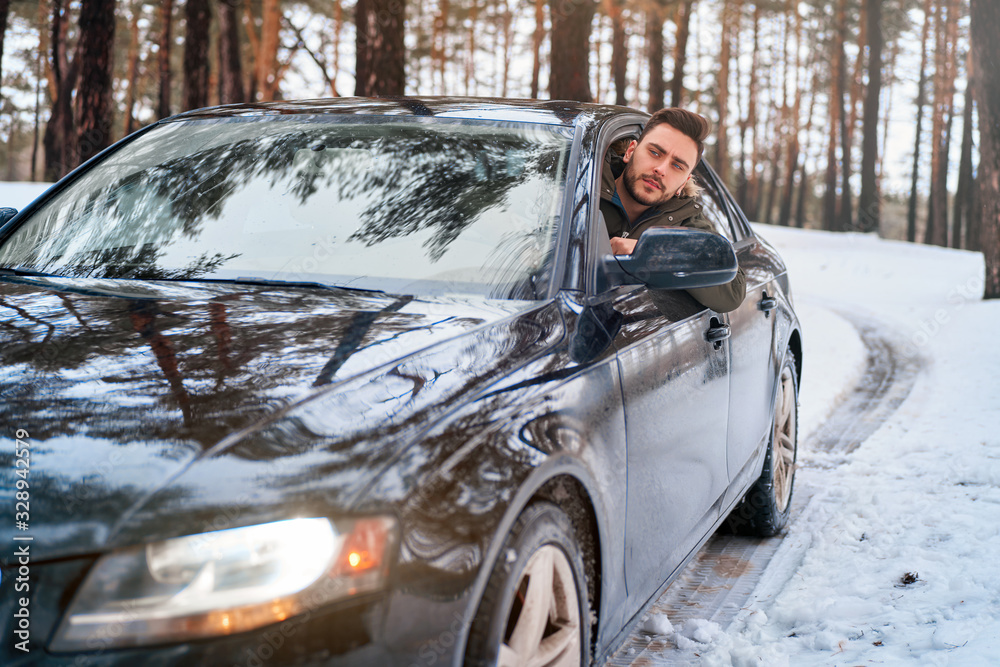 Young attractive Caucasian man sits at the wheel of his car sunny winter day. Young attractive Caucasian man sits at the wheel of his car sunny winter day.