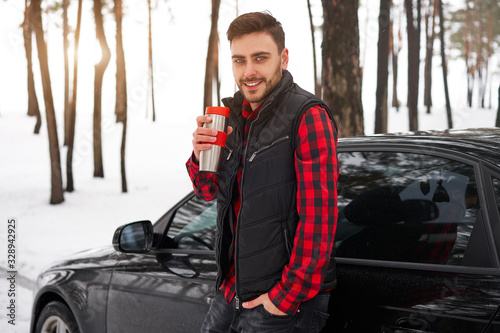 Attractive Caucasian man stands in winter forest near his car.