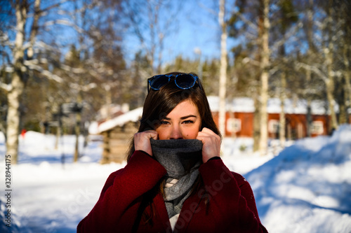 A female model smiling and enjoying sunny winter weather outdoor wearing a scarf and a sunglass as a fashion statement