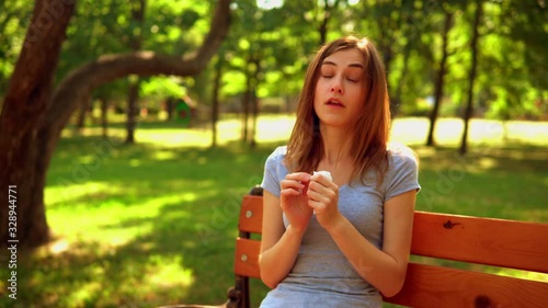 young woman sitting on the bench in park summer season holding a napkin and sneezing seasonal allergies photo