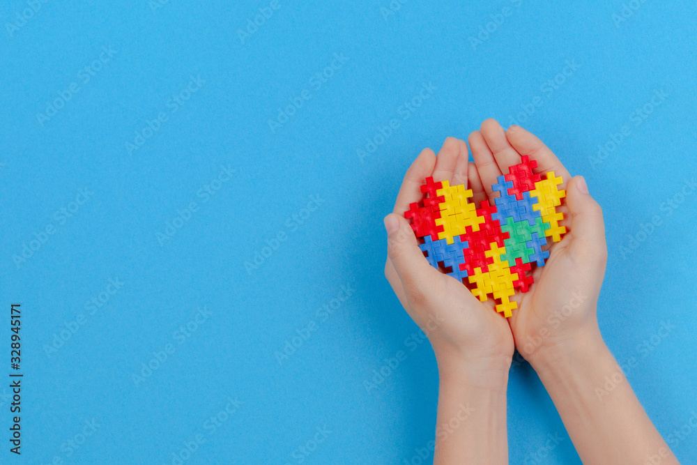 Kid hand holding colorful heart on light blue background. World autism awareness day concept Kid hand holding colorful heart on light blue background. World autism awareness day concept