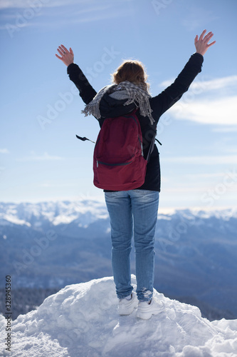 The girl on the snowy peak raised her hands up. A traveler at a mountain ski resort stands on the edge. A man on top. Winter weather. 