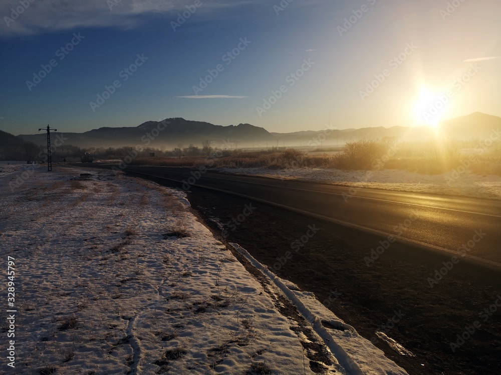 Winter road in the morning. Sunrise over the mountains