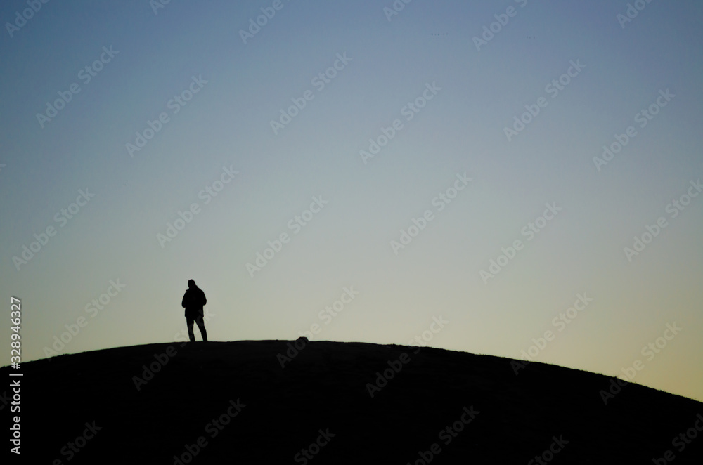 Silhouette of a person placed on top of a hill during a sunrise