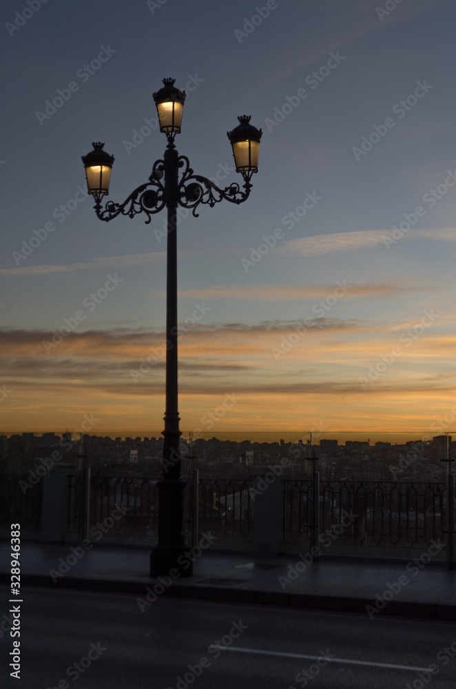 Old lamppost with its streetlights on during a sunset full of warm colors